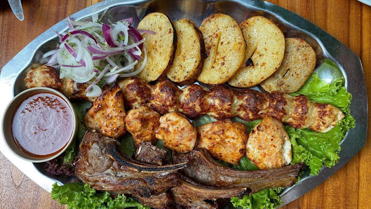 A plated dish featuring grilled skewers of meat and chicken pieces accompanied by roasted potatoes, a side salad with onions and lettuce, and a small