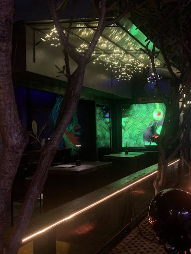 This image depicts an interior view of a modern bar or lounge area at night. The space is dimly lit with ambient green lighting, creating a moody atmo