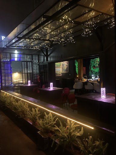 The image depicts an indoor dining area at night, featuring a modern and stylish ambiance with hanging lights that create a warm glow. The space is pa