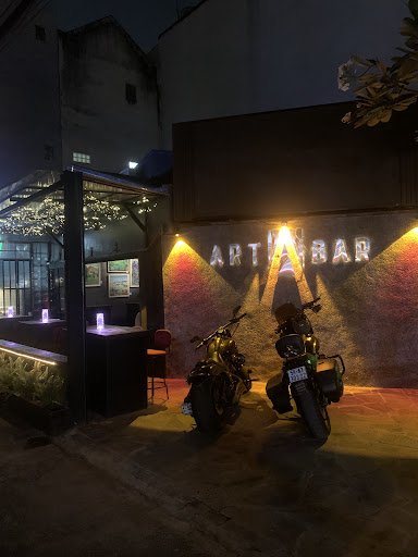 The image shows an exterior view of a bar named 'ART BAR' at night time with two motorcycles parked in front, illuminated by warm lights.