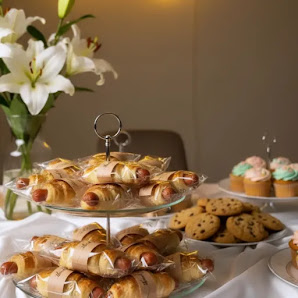The image shows a display of pastries and desserts on tiered stands in what appears to be an elegant venue with white flowers as decoration.