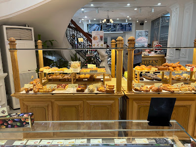 The image shows an interior view of a bakery or café in Thao Dien, Saigon with various pastries and baked goods displayed on wooden counters.