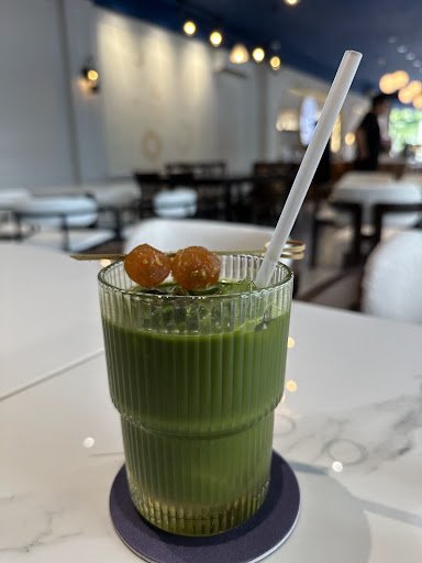 A green smoothie or juice in a ribbed glass on a coaster, garnished with two round brown fruits and served with a white straw.