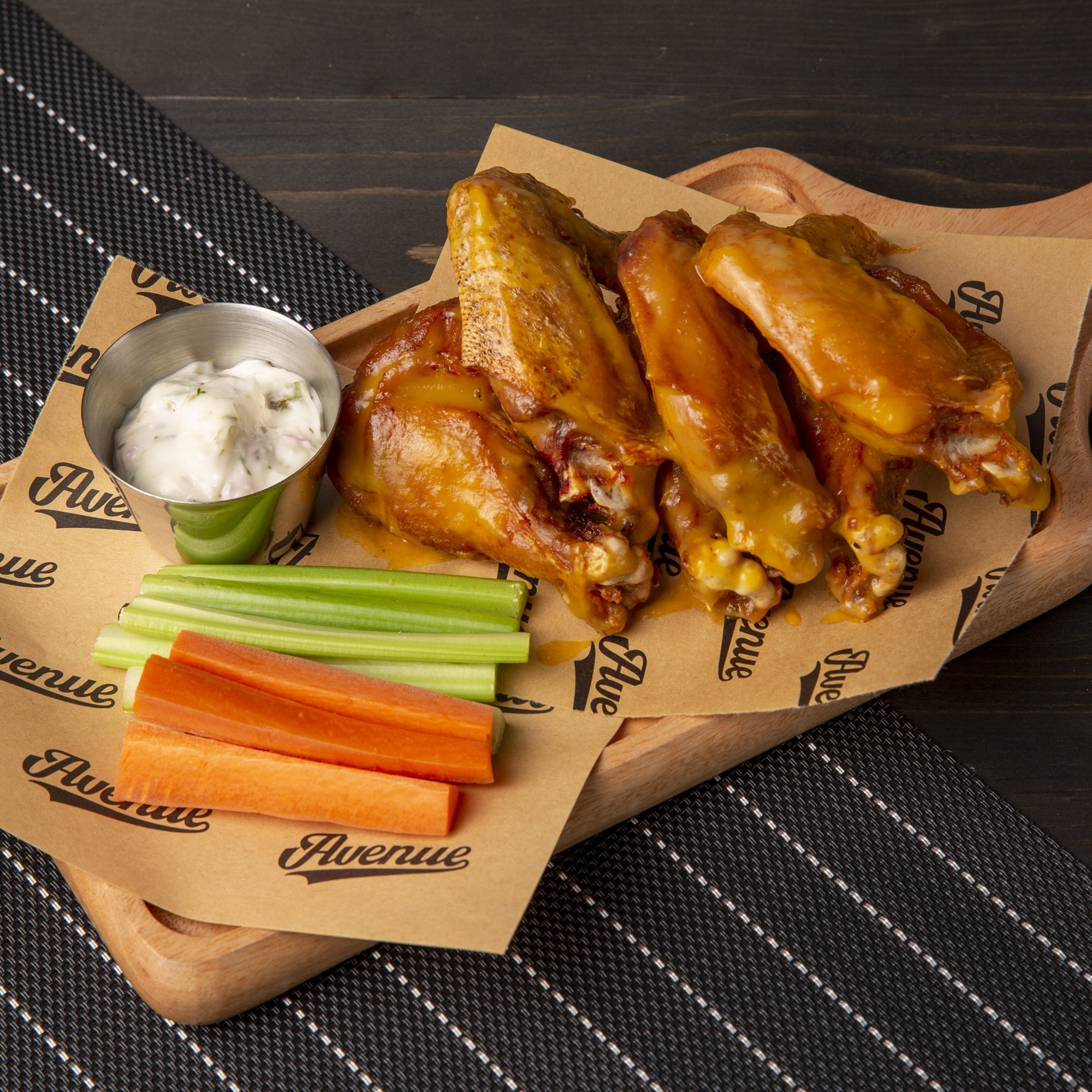 A close-up of a serving tray containing chicken wings coated in sauce, accompanied by celery sticks and carrot sticks with dip on the side.