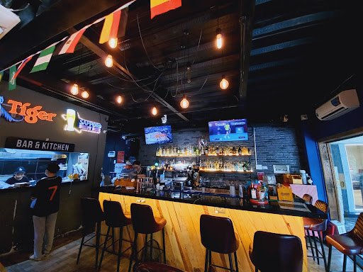 The image shows an interior view of a bar named 'Tiger Bar & Kitchen'. The establishment has a modern and cozy ambiance with wooden accents, hanging l