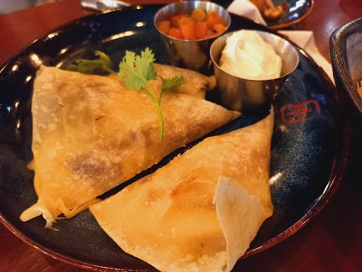 The image shows a plated dish consisting of two pieces of what appears to be quesadillas or similar flatbreads, accompanied by small bowls containing 