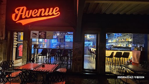 The image shows an exterior view of a bar or restaurant named 'Avenue' at night time with neon signage above the entrance, and outdoor seating visible