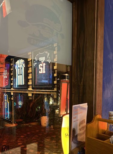 The image shows an interior view of a sports-themed bar or restaurant featuring framed jerseys on display and promotional materials for beer brands su