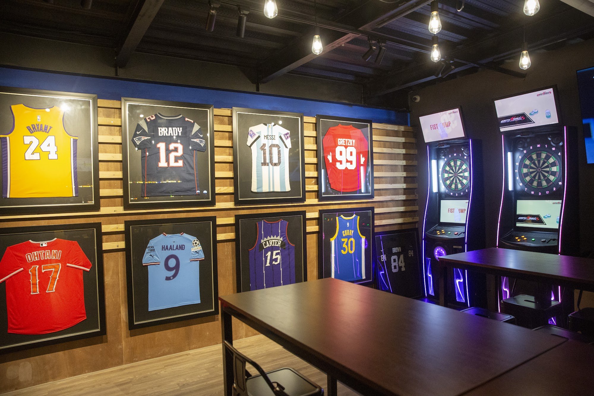 The image shows an interior space that appears to be a sports bar or gaming lounge with various framed jerseys displayed on the wall, including those 