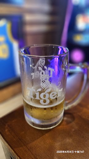 A close-up of a glass mug labeled 'Tiger' containing beer on a wooden surface with blurred neon lights in the background, suggesting it is taken insid
