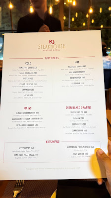 The image shows a printed menu from 'B3 STEAKHOUSE' held by a person in a restaurant setting. The menu features sections labeled 'COOL', 'HOT', 'SEA',
