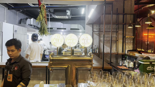 The image depicts an interior view of a modern bar or brewery setting in Thao Dien, Saigon. The focus is on the central brewing equipment with taps la