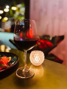 A close-up shot of a glass of red wine on a table in an indoor setting with warm lighting and ambient decor, including a lit candle holder.