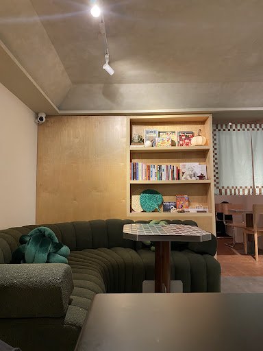 The image shows a cozy interior space featuring a green sectional sofa and wooden bookshelves filled with books and decorative items, including colorf