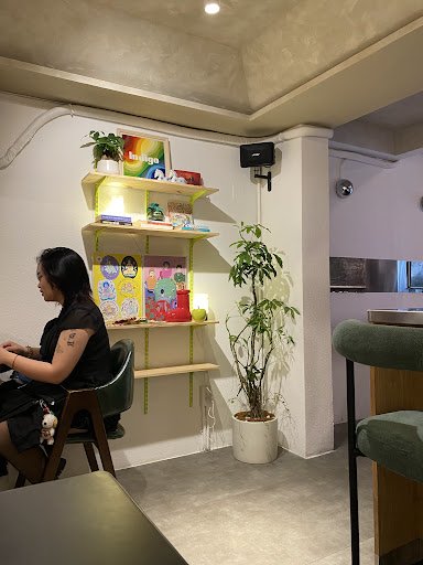 The image shows an interior space of a modern cafe or restaurant in Thao Dien, Saigon. A woman is seated at a table with her back to the camera, focus