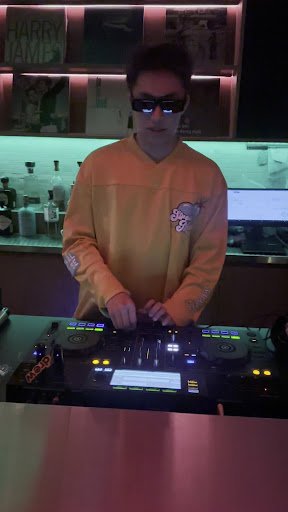 A DJ is operating a turntable setup in what appears to be an indoor venue, possibly during nighttime given the ambient lighting and mood.