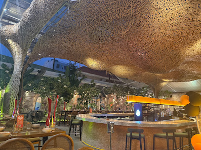 The image depicts the interior of a contemporary venue in Thao Dien, Saigon. Features include a central bar with stools, wooden tables and chairs, a l