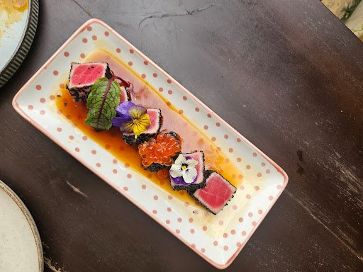 A plated dish featuring a gourmet presentation of what appears to be tuna tartare or sashimi with garnishes such as edible flowers and caviar, served