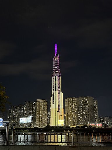 The image captures a nighttime view of an illuminated skyscraper in the center, standing prominently against a dark sky with city lights visible aroun