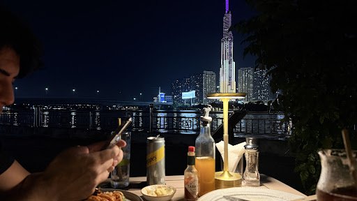 A person is seated at a table outdoors during nighttime overlooking an urban skyline and the illuminated Burj Khalifa in Dubai, United Arab Emirates.