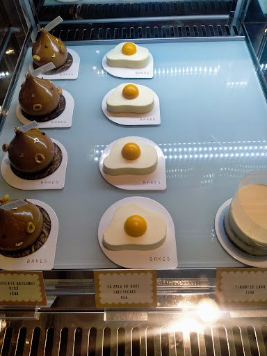 A display case in a bakery or dessert shop showcasing an assortment of creatively designed cakes and pastries that resemble various animals and object