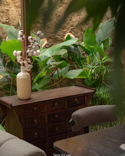 The image depicts an interior setting that appears cozy and inviting, featuring a wooden chest of drawers with multiple compartments on which sits a v