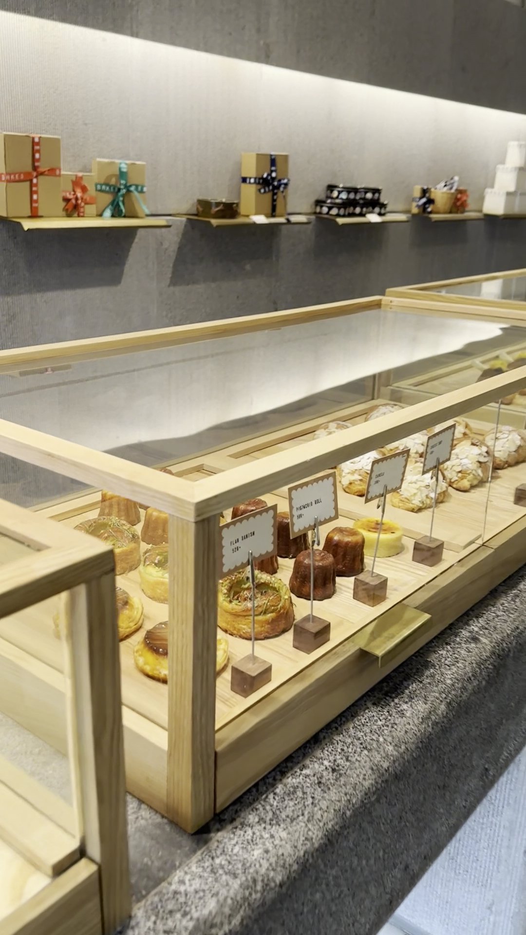 The image depicts the interior of a bakery or café in Thao Dien, Saigon, featuring a wooden display case with glass front showcasing various pastries