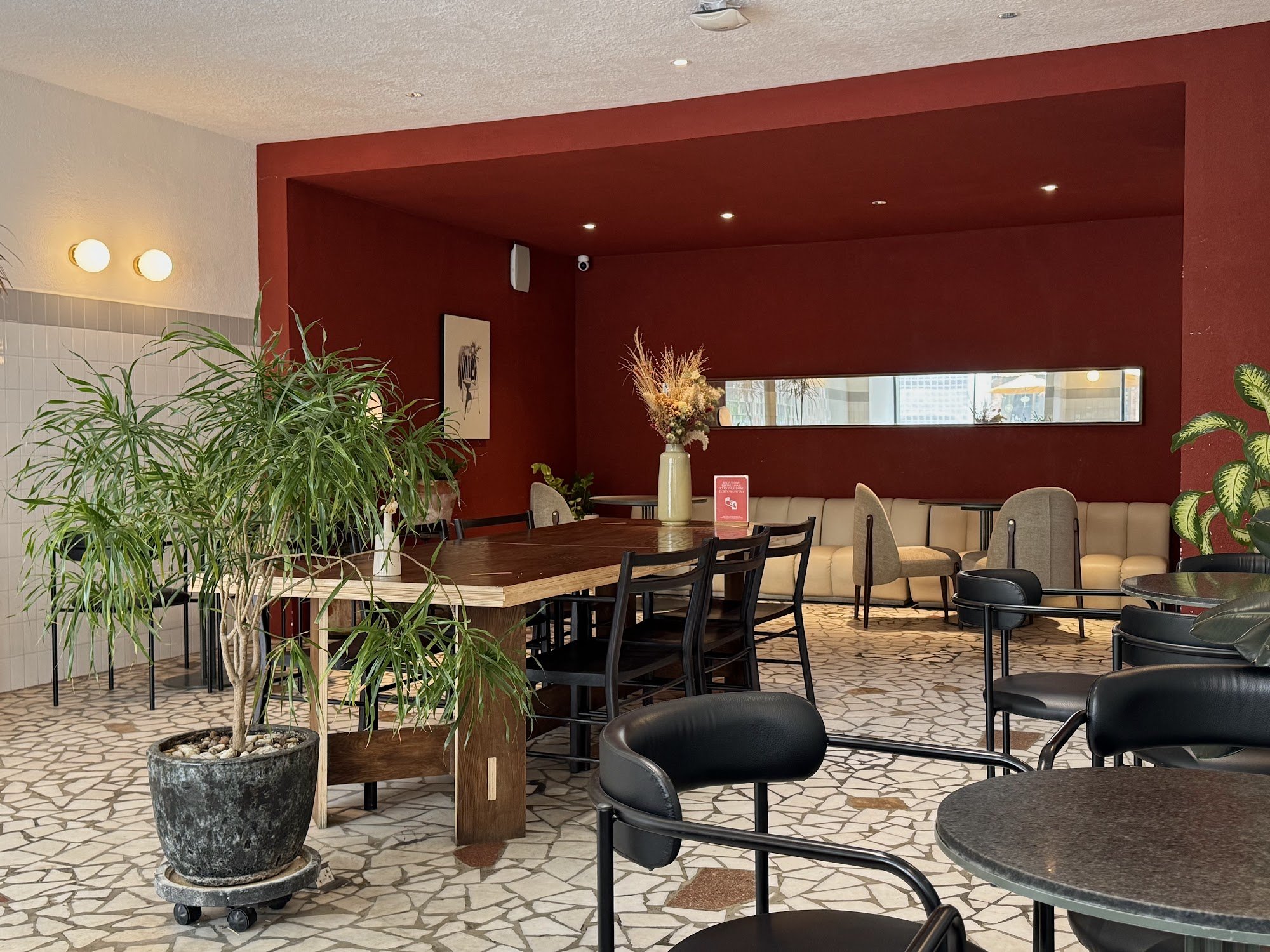 The image depicts the interior of a modern venue in Thao Dien, Saigon. It features a large wooden table surrounded by black chairs, with a potted plan