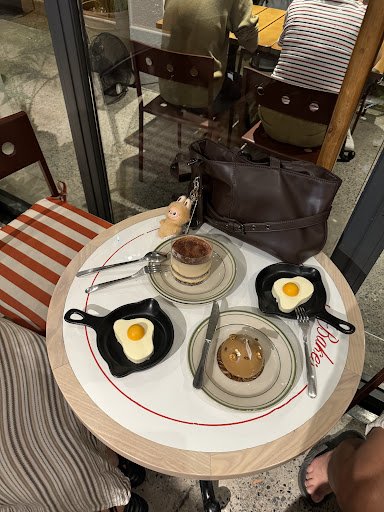 The image shows a table in an indoor cafe setting with various breakfast items including eggs and pancakes served on plates alongside black ceramic eg