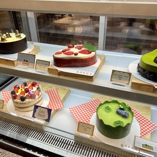 A display case in a bakery or dessert shop showcasing an assortment of cakes and desserts on red checkered paper with labels indicating they are for s