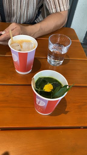 The image shows a table setting in what appears to be an indoor venue, possibly Thao Dien, Saigon. There are three drinks on the wooden table: two red