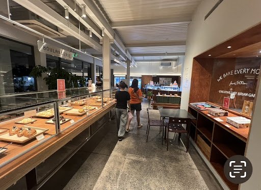 The image depicts the interior of a modern bakery or café in Thao Dien, Saigon. It features a long display counter with various baked goods (pastries,