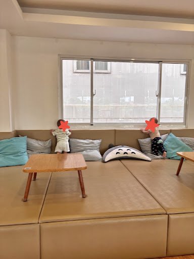 The image shows a cozy interior setting featuring two plush toys sitting on a large beige sofa with multiple cushions and pillows in various colors, i