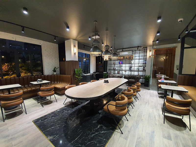 The image depicts a modern restaurant interior in Thao Dien, Saigon. It features a large oval table with brown leather chairs, a marble-tiled area, an