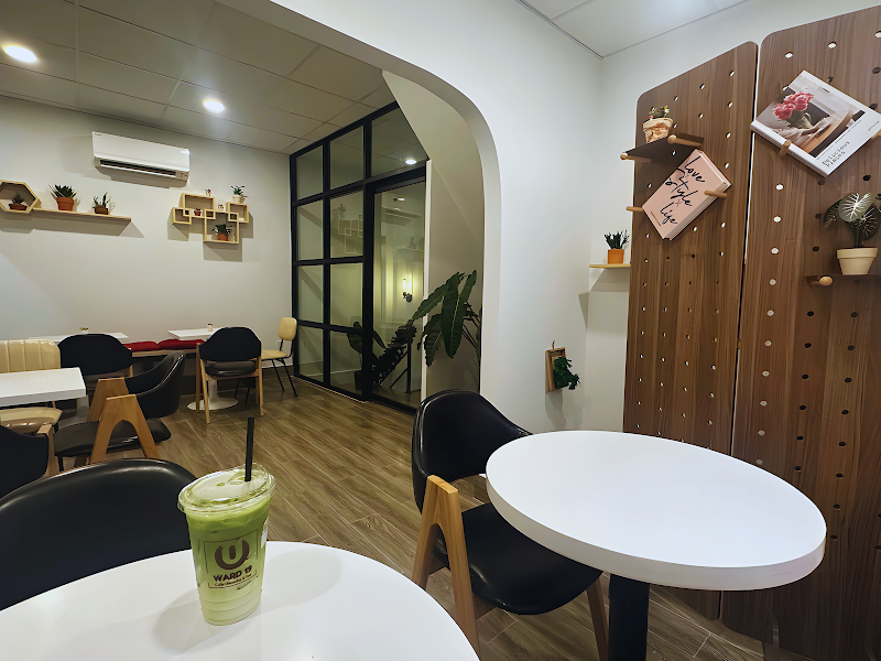A modern café interior in Thao Dien, Saigon. Features white round tables, black chairs with wooden legs, a green drink with a straw on a table, wooden