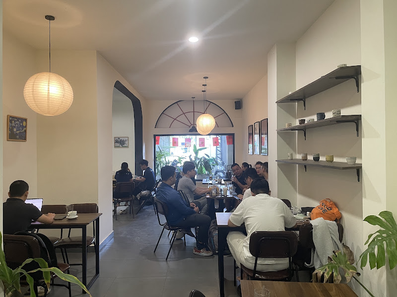 The image depicts the interior of a modern café or restaurant in Thao Dien, Saigon. It features a spacious layout with several tables and chairs occup