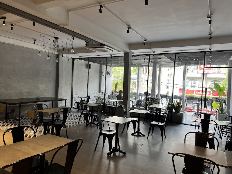 Interior of a modern café in Thao Dien, Saigon. Features industrial-style design with exposed concrete walls, black metal chairs and tables, large gla