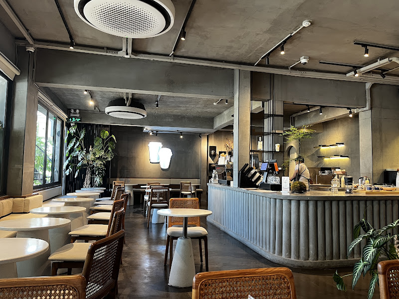 The image depicts the interior of a modern café in Thao Dien, Saigon. It features an industrial-chic design with exposed concrete ceilings, visible pi