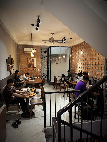 The image depicts the interior of a café or restaurant in Thao Dien, Saigon. It features multiple tables with patrons seated, some working on laptops.