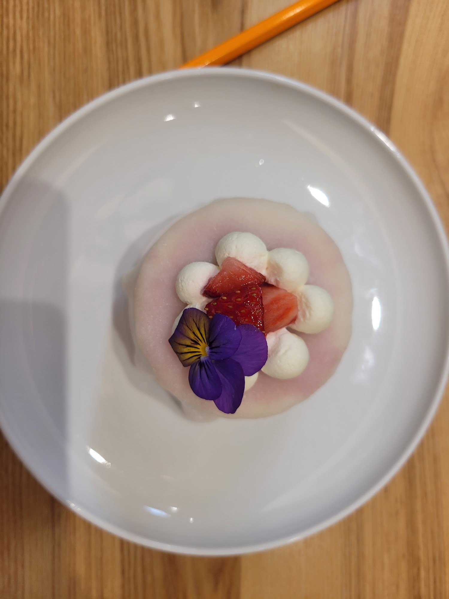 A dessert dish presented on a white plate featuring what appears to be a scoop of pink sorbet or mousse with several dollops of whipped cream, topped 