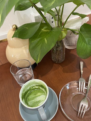 The image shows a part of an interior setting that includes a wooden table on which various items are placed such as a cup with green tea, glasses con