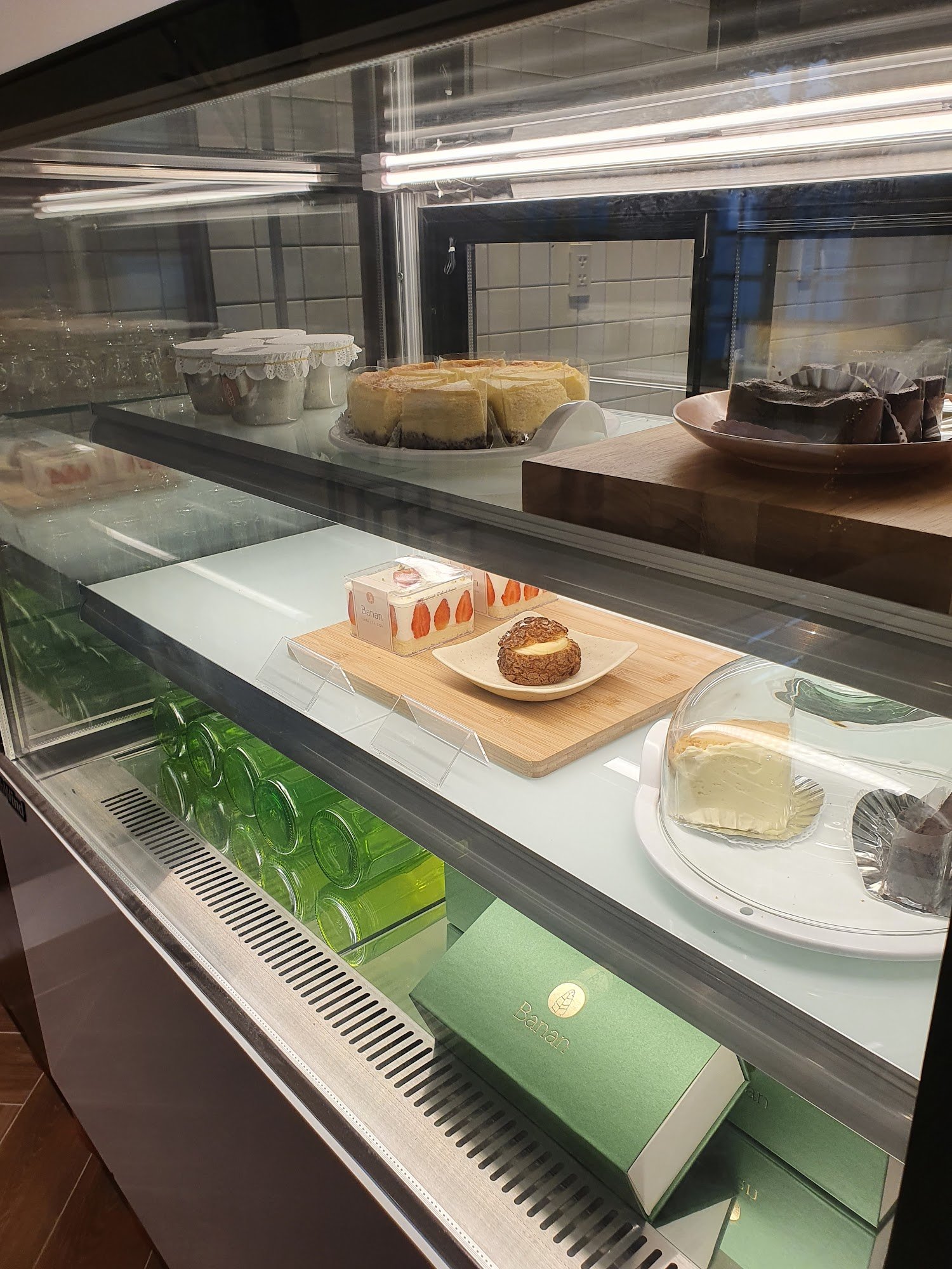 The image shows a display case in what appears to be a bakery or dessert shop with various cakes and pastries on shelves, illuminated by fluorescent l