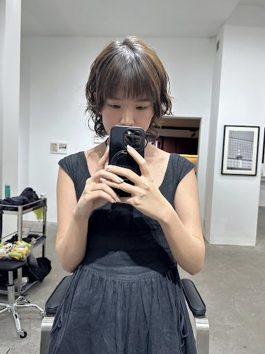 A woman is taking a selfie in what appears to be an interior space of Thao Dien, Saigon. She stands before a mirror with her reflection captured on th