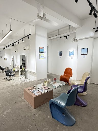 The image depicts an interior space that appears to be a modern salon or gallery. The room is spacious with white walls and features several pieces of