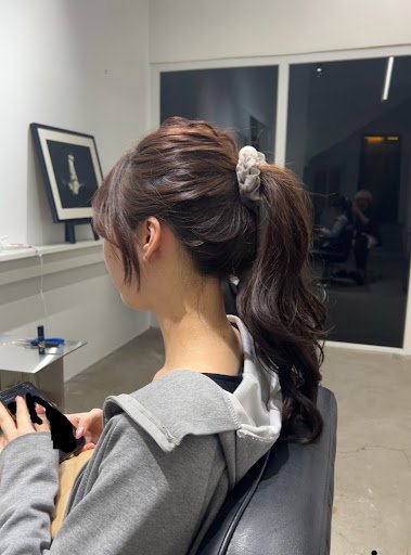 A person is seated in a salon chair looking at their phone while waiting for services.