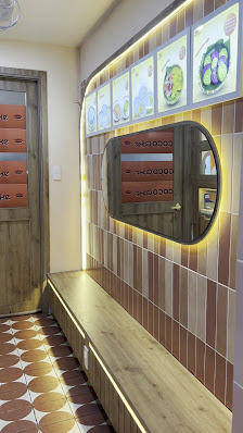 The image shows an interior view of a restaurant or cafe featuring brown and beige tiled walls with decorative plates above them. A wooden bench is vi