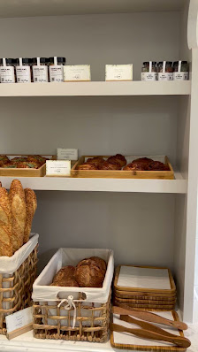 The image shows a neatly organized display of baked goods on shelves and in baskets within an interior setting that appears to be part of a bakery or