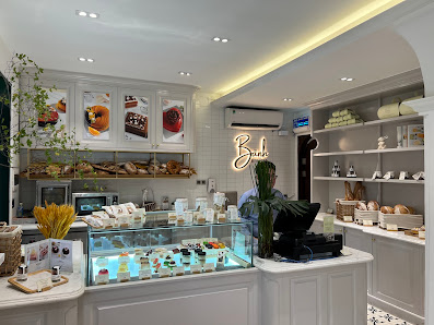 The image shows a well-lit and modern interior of what appears to be a bakery or café with various baked goods on display in the background, including