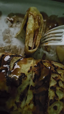A close-up of a plated dessert consisting of caramelized bananas and what appears to be crepes or pancakes with a glossy, syrupy topping.