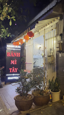 The image shows an exterior view of a restaurant at night time. The entrance is adorned with red lanterns and potted plants, leading to the name 'Bánh